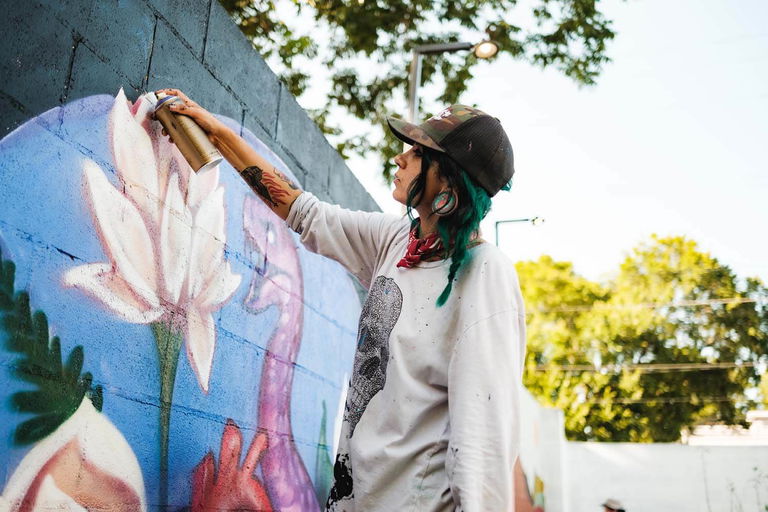 Young woman in baseball cap spray painting on art wall