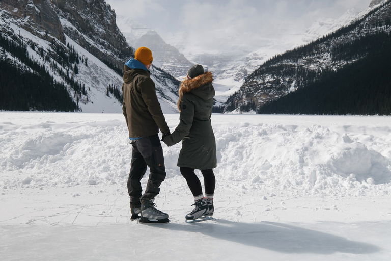 Man and woman hold hands while looking out across a snowy mountainous valley