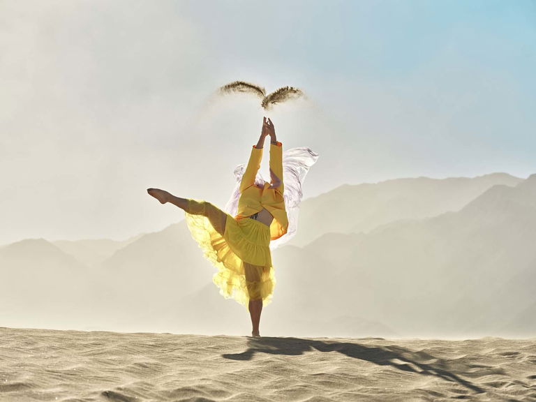 Clad in a banana chiffron suit-dress, a man poses, tossing sand into the air